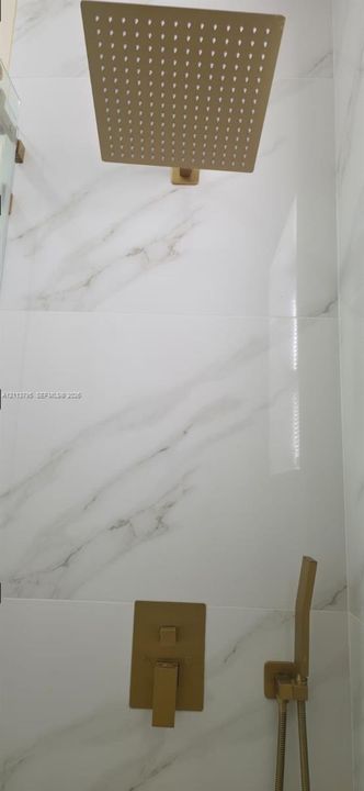 Shower enclosure featuring large-format veined porcelain tile, a gold-tone rainfall showerhead, and a matching gold-tone handheld sprayer with wall-mounted control hardware