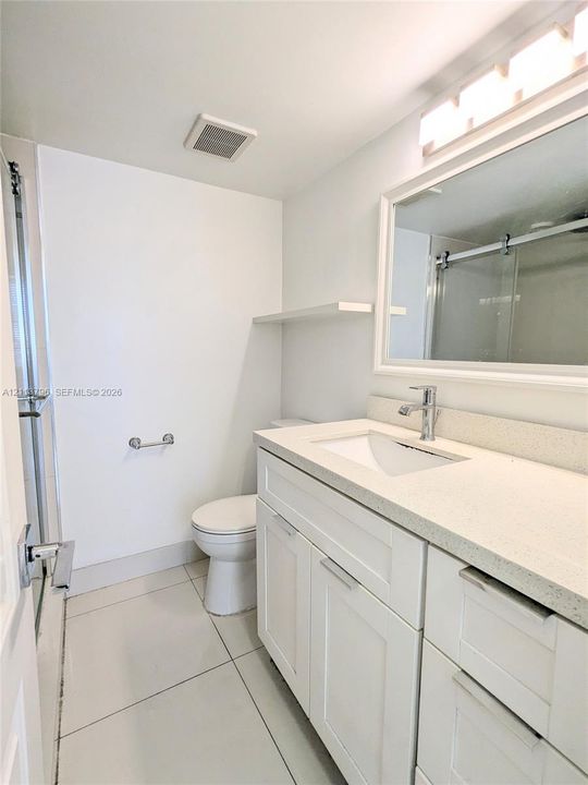 Bathroom featuring a white shaker-style vanity with stone-composite countertop, integrated rectangular sink, framed mirror, and tiled flooring