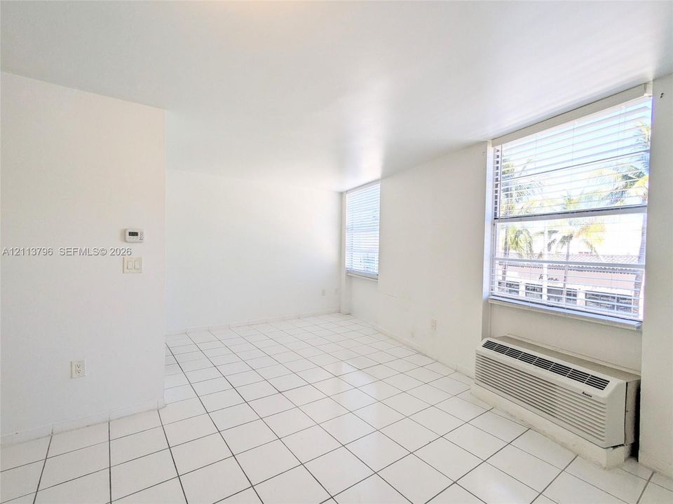 Interior space featuring white tiled flooring, large windows with horizontal blinds, and a built-in wall-mounted heating and cooling unit