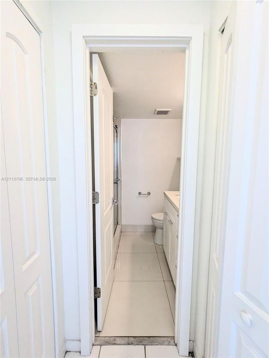 Bathroom featuring large-format ceramic tile flooring, a white vanity cabinet with an integrated countertop, and a walk-in shower enclosure