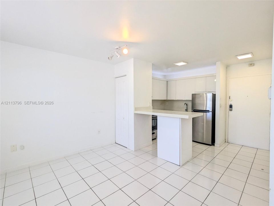 Interior space featuring white tile flooring, neutral walls, dual windows with horizontal blinds, and a built-in wall-mounted climate control unit