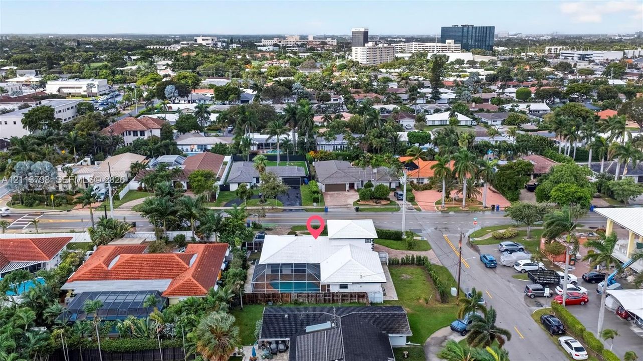 Aerial perspective featuring a white-roofed residence with a screen-enclosed pool, perimeter fencing, and established palm trees in a residential neighborhood