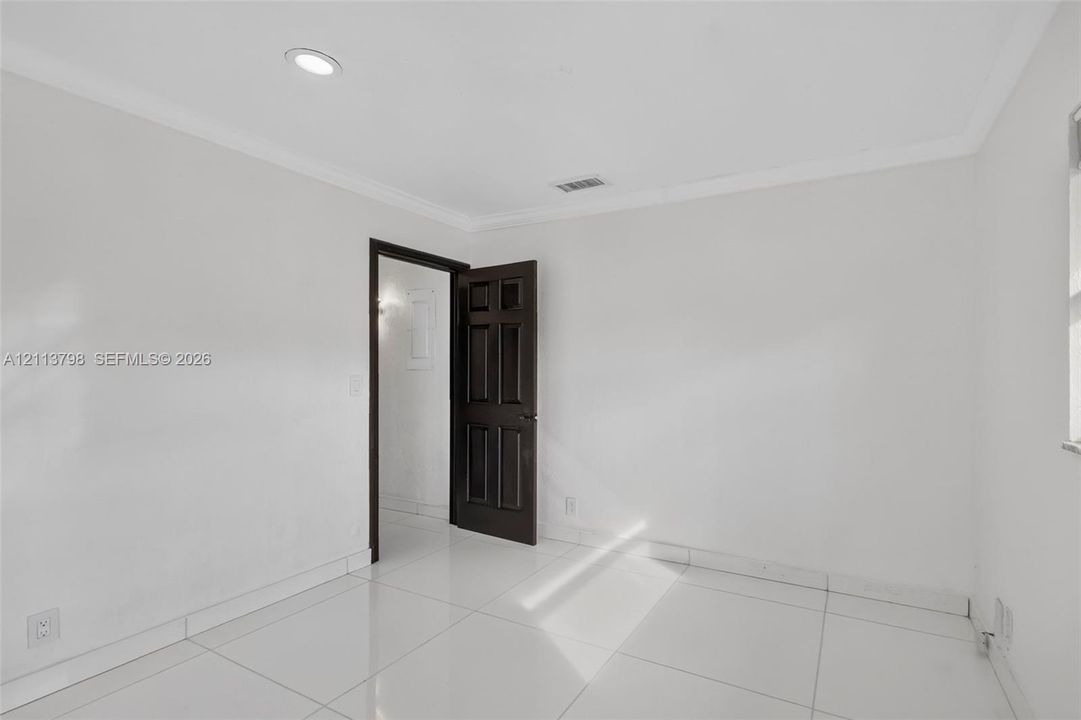 Interior room featuring large-format tile flooring, crown molding, recessed lighting, and a six-panel dark wood-finish door
