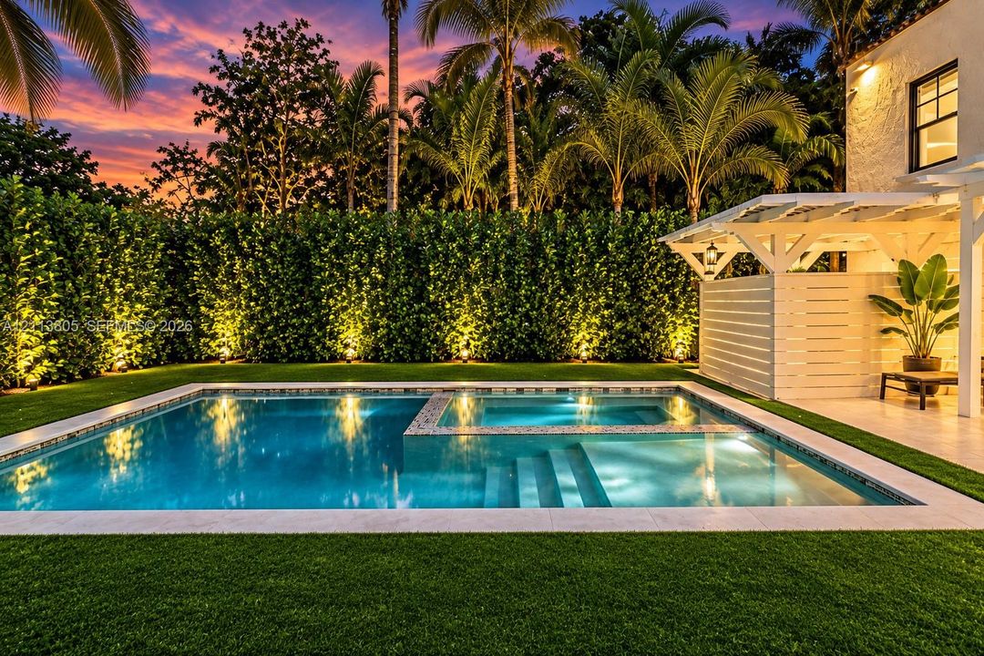 Outdoor pool with an integrated spa, stone coping, manicured turf, white pergola, and privacy hedging