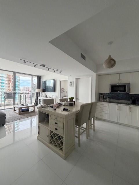 Open-concept living space featuring high-gloss tile flooring, floor-to-ceiling glass panel doors, a kitchen island with built-in wine storage, recessed track lighting, and shaker-style cabinetry