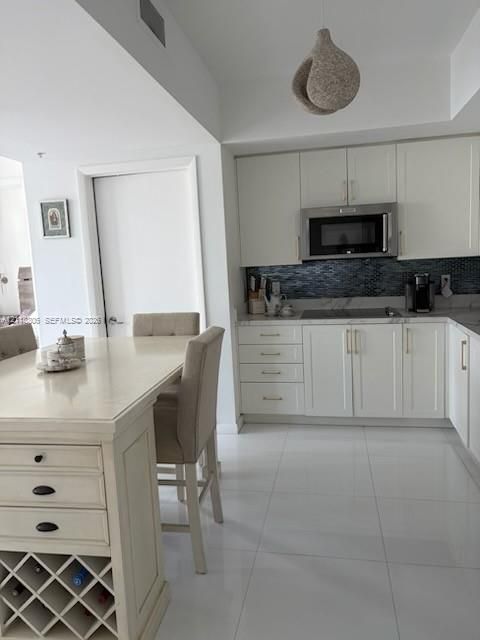 Kitchen featuring shaker-style cabinetry, stainless steel microwave, stone-finish countertops, tile backsplash, and built-in wine storage