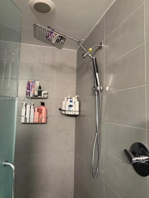 Shower enclosure featuring large-format grey wall tiling, a rainfall showerhead, a detachable hand-held sprayer, and a single-handle temperature control valve