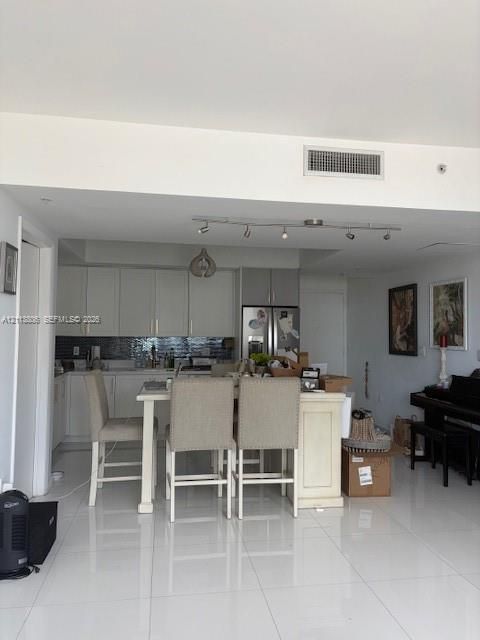Kitchen featuring white cabinetry, a tiled backsplash, a central island, track lighting, and white tile flooring