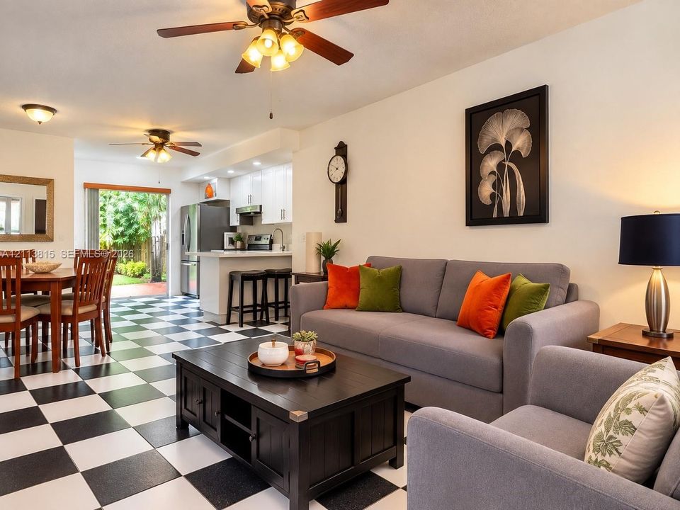 Open-concept living space featuring high-contrast checkerboard tile flooring, white cabinetry, integrated peninsula breakfast bar, and multiple ceiling-mounted light fixtures