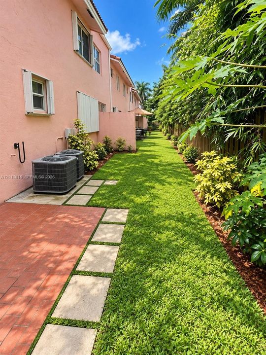 Exterior grounds featuring a paved brick patio, square concrete pavers, a manicured lawn, perimeter landscaping, and privacy fencing