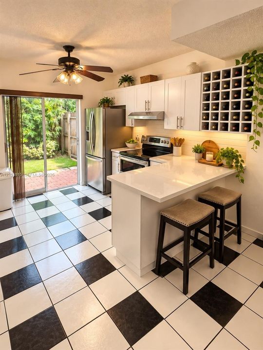 Kitchen featuring white cabinetry, a built-in wine rack, stone-surfaced countertops, stainless steel appliances, and checkered tile flooring