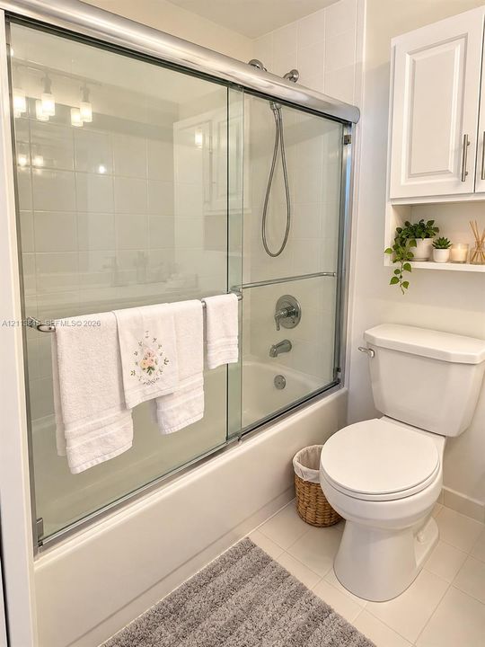 Full-size tub with sliding glass enclosure, white ceramic tile surround, chrome shower hardware, and white built-in wall cabinetry
