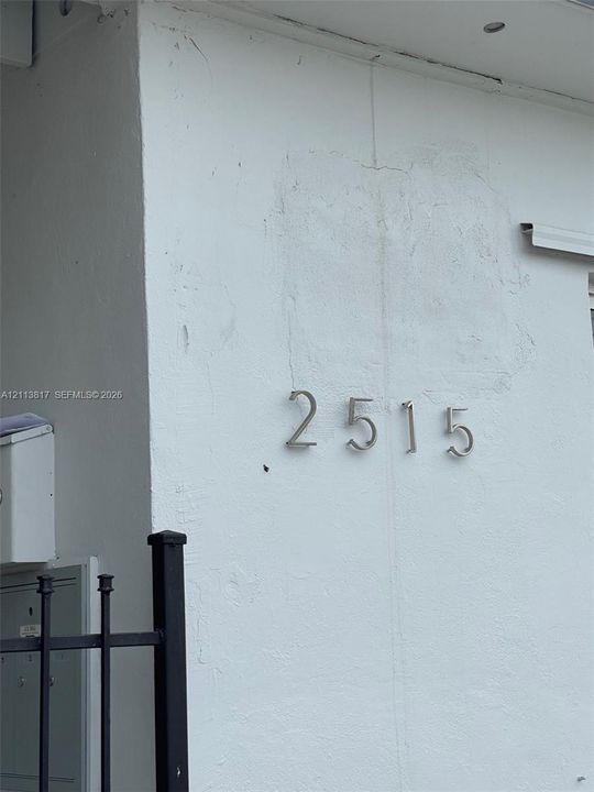 Exterior wall featuring smooth white stucco finish, brushed metal house numbers, and black metal fencing