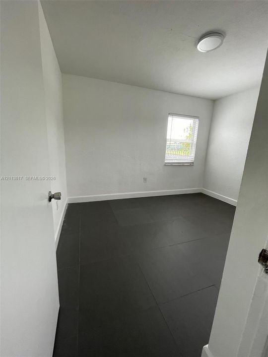 Interior room featuring dark large-format tile flooring, white wall finishes, a single-pane window with horizontal blinds, and a flush-mount ceiling light fixture