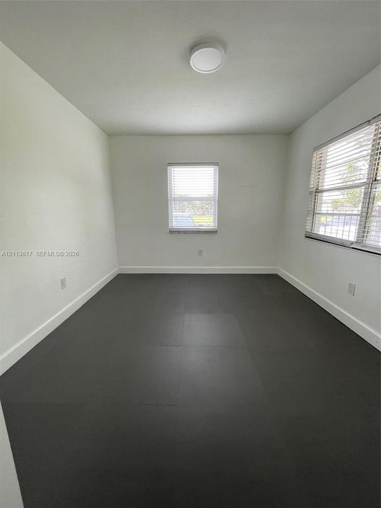 Neutral-toned interior space featuring dark grey tile flooring, bright white walls, two multi-pane windows with horizontal blinds, and a flush-mount ceiling light fixture