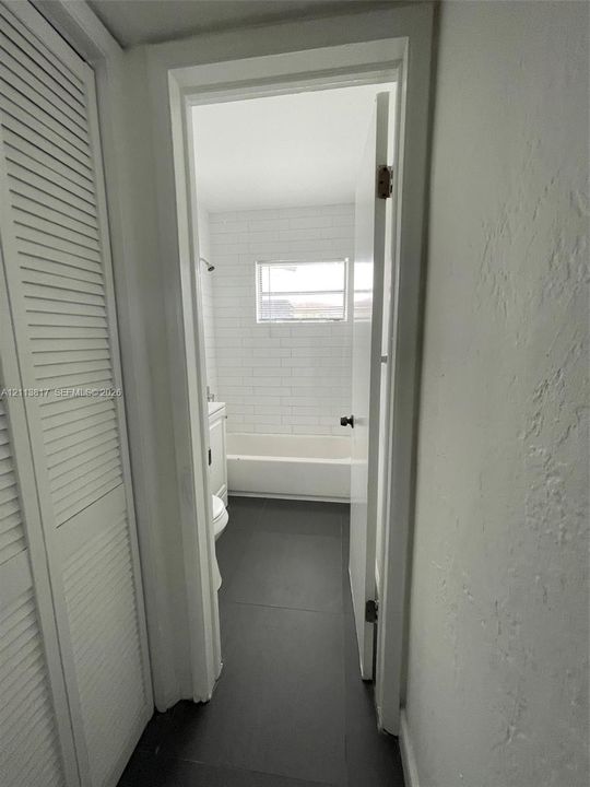 Bathroom featuring large-format dark floor tile, white subway tile shower surround, and louvered-style closet doors