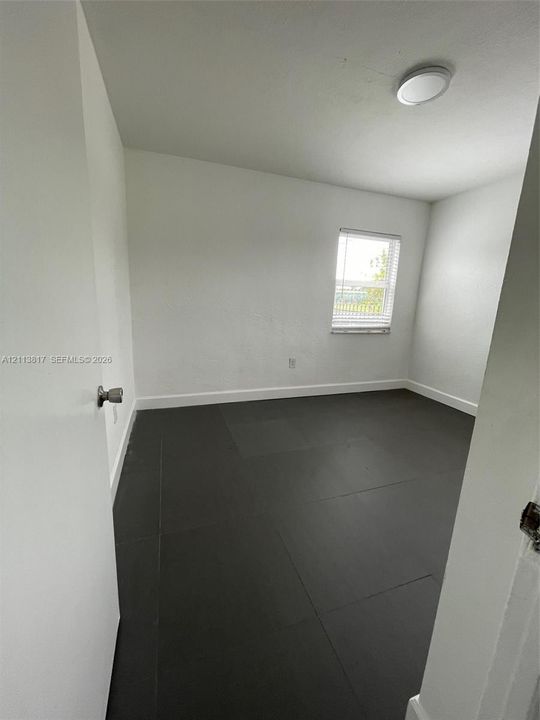 Neutral wall tones, dark tile flooring, a single-pane window, and a flush-mount overhead light fixture