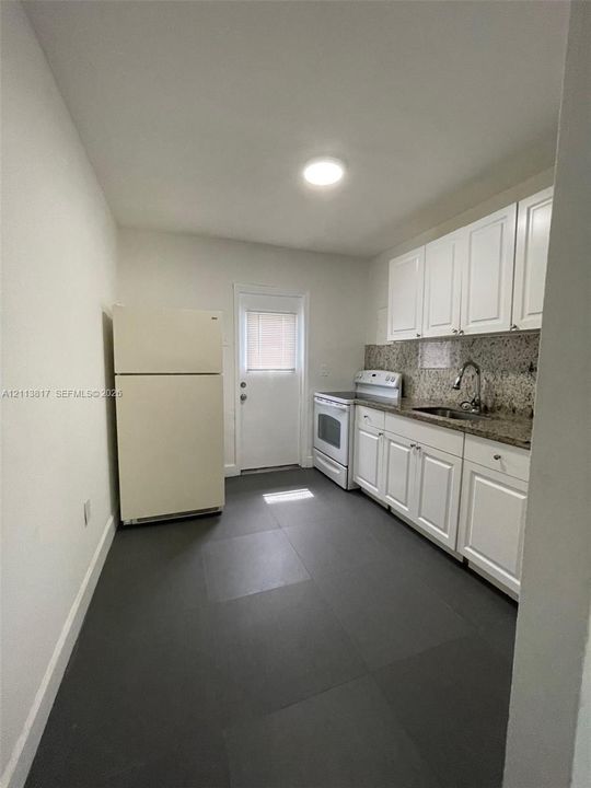 Kitchen featuring white cabinetry, stone-finish countertops, dark large-format tile flooring, a stainless steel sink with a high-arch faucet, and an exterior door