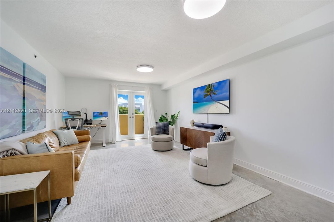 Neutral-toned interior space featuring polished concrete flooring, white walls, and French doors providing access to an exterior balcony