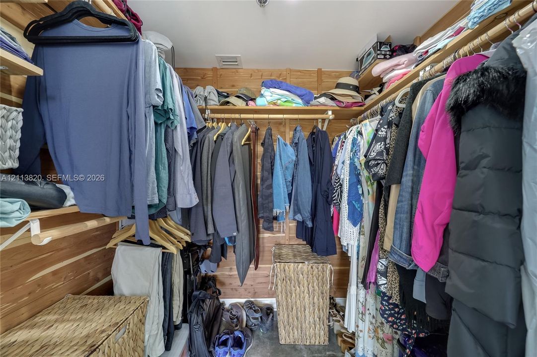 Walk-in closet featuring natural wood-paneled walls and tiered wooden shelving with integrated hanging rods
