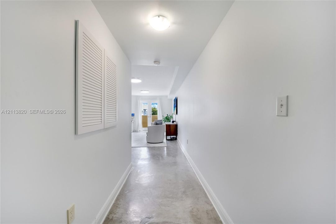Hallway featuring polished concrete flooring, white walls, louvered closet doors, and flush-mount ceiling lighting