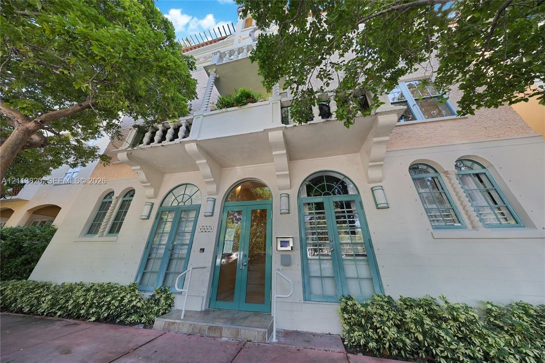 Mediterranean-inspired exterior featuring stucco facade, arched multi-pane glass entry doors, second-story balcony with decorative balustrade, and symmetrical arched window detailing