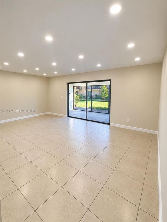 Neutral-toned ceramic tile flooring, recessed ceiling lighting, and sliding glass doors with dark frames opening to a screened-in patio area