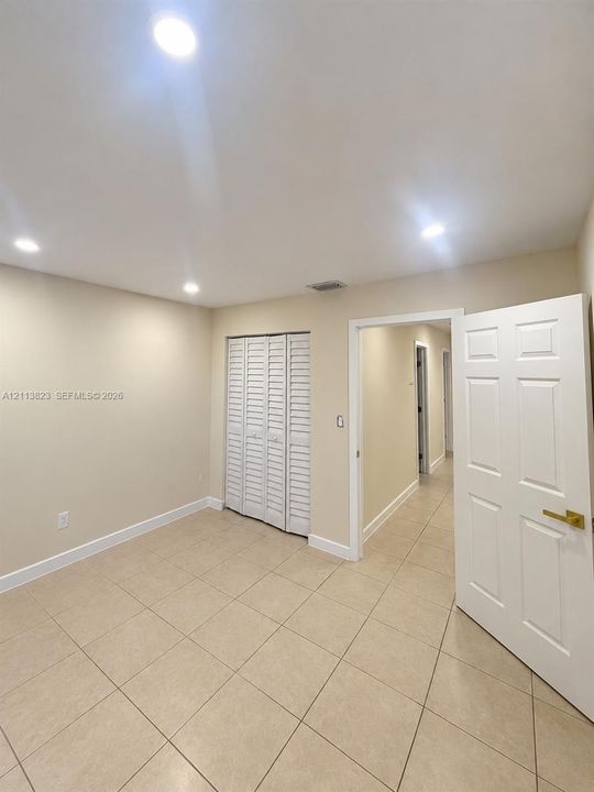 Neutral-toned interior featuring large-format ceramic floor tile, recessed ceiling lighting, and louvered-style closet doors