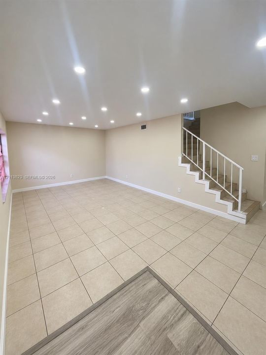 Open-concept interior featuring neutral ceramic tile flooring, recessed ceiling lighting, and a staircase with a white metal railing