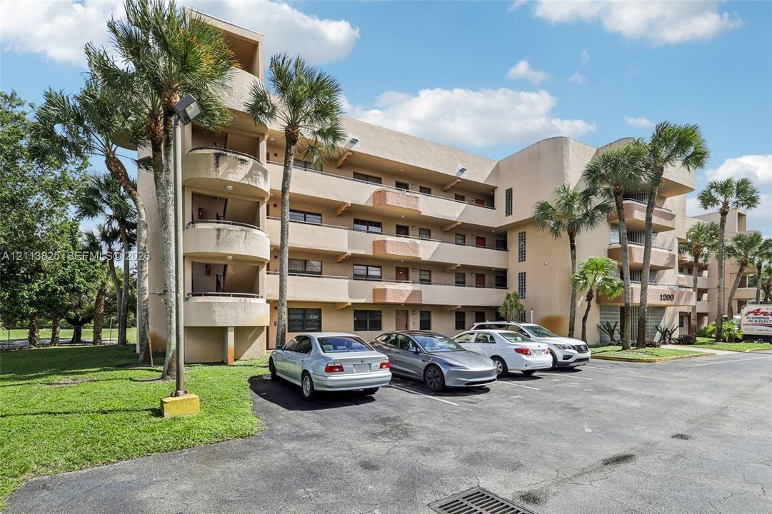 Multi-story residential building featuring stucco exterior, private curved balconies, and mature palm tree landscaping