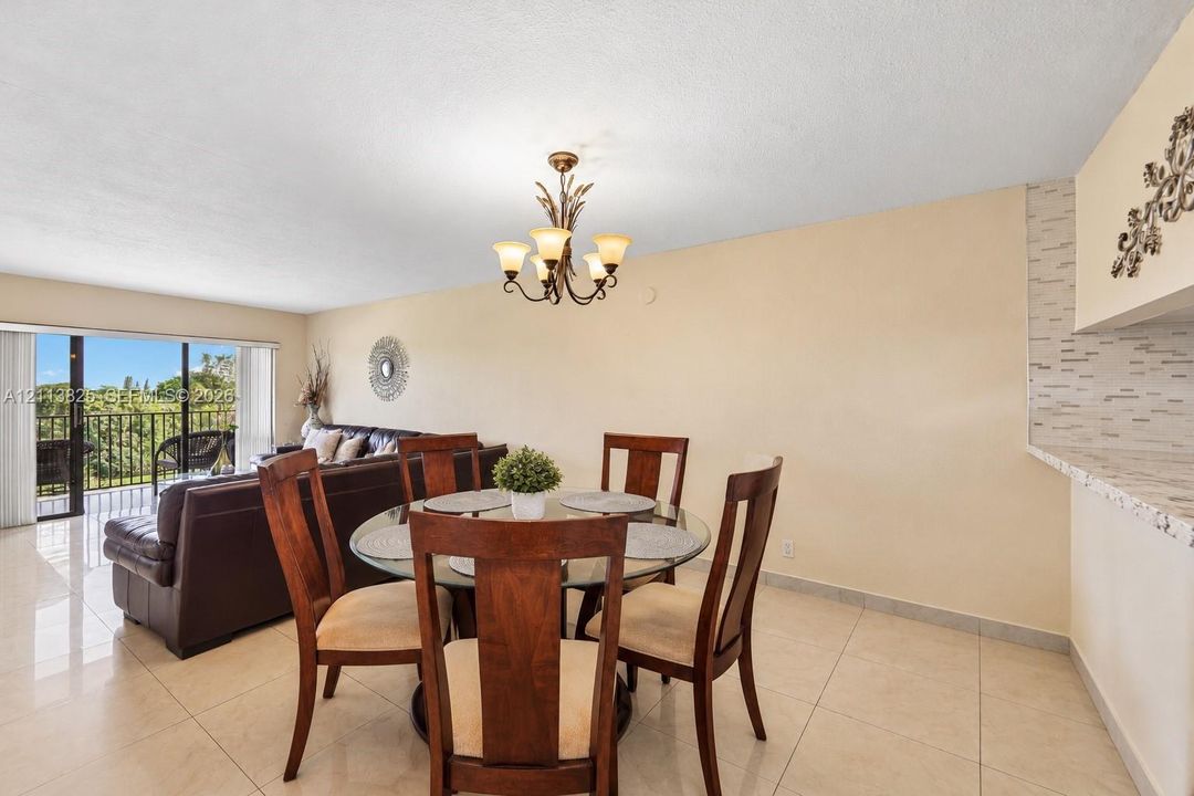 Open-concept area featuring tile flooring, a multi-arm chandelier, and a breakfast bar with stone-finish surfacing and decorative tile backsplash