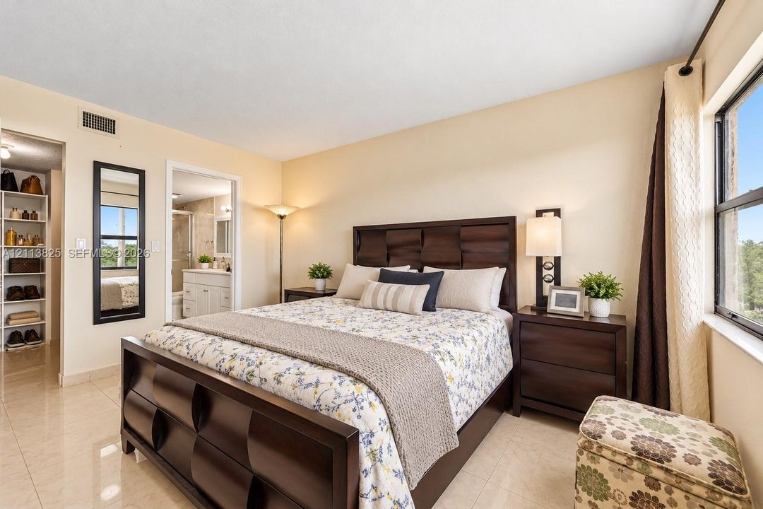 Spacious room featuring neutral tile flooring, a wall-mounted rectangular mirror with a dark frame, and a walk-in storage area with built-in shelving