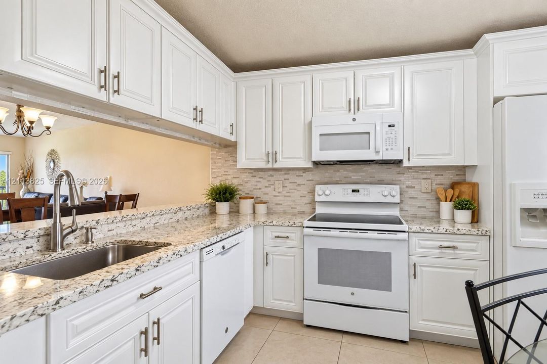 Kitchen featuring white shaker-style cabinetry, speckled stone countertops, a subway tile backsplash, and stainless steel undermount sink