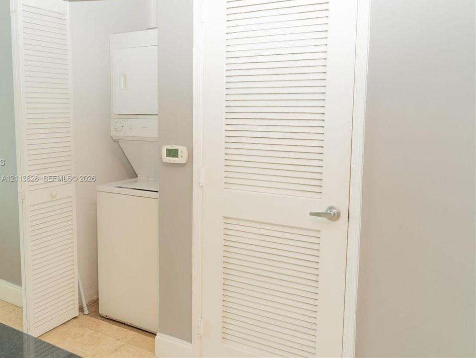 Laundry area featuring a stacked washer and dryer unit enclosed by white louvered doors