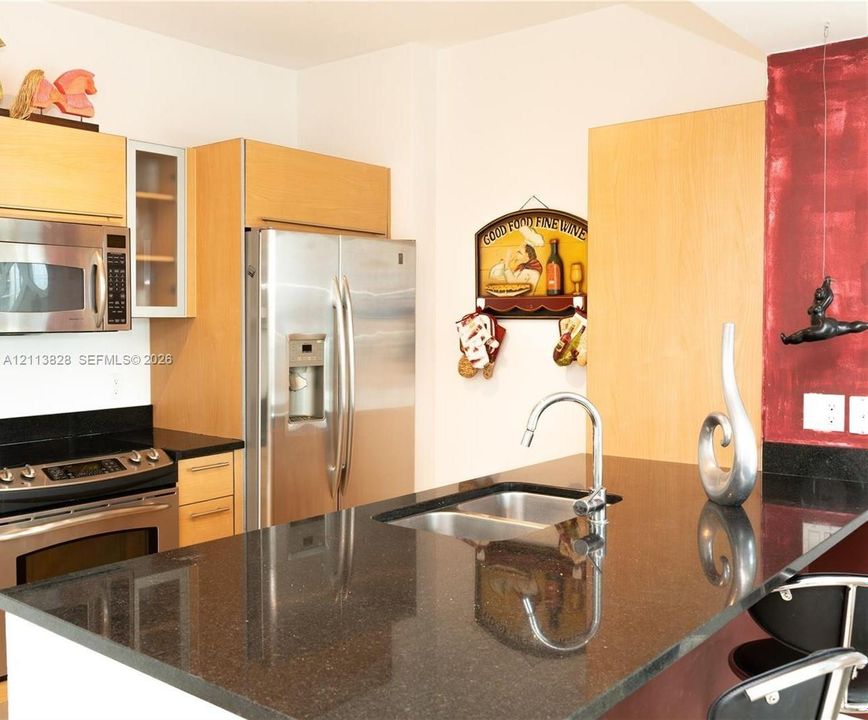 Kitchen featuring flat-panel wood-finish cabinetry, black stone countertops, stainless steel side-by-side refrigerator, built-in microwave, and stainless steel dual-basin sink with a gooseneck faucet