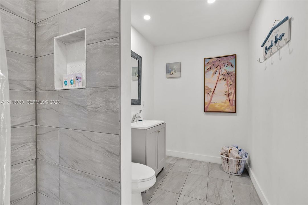 Bathroom featuring large-format grey tile shower surround with integrated wall niche, light grey vanity cabinet, solid-surface countertop, and ceramic floor tiling