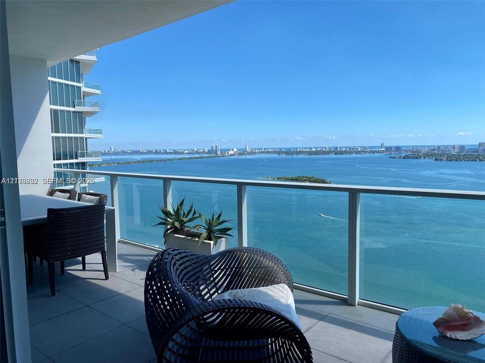 Covered balcony featuring oversized tile flooring and a glass-panel railing, offering unobstructed water and coastal scenery