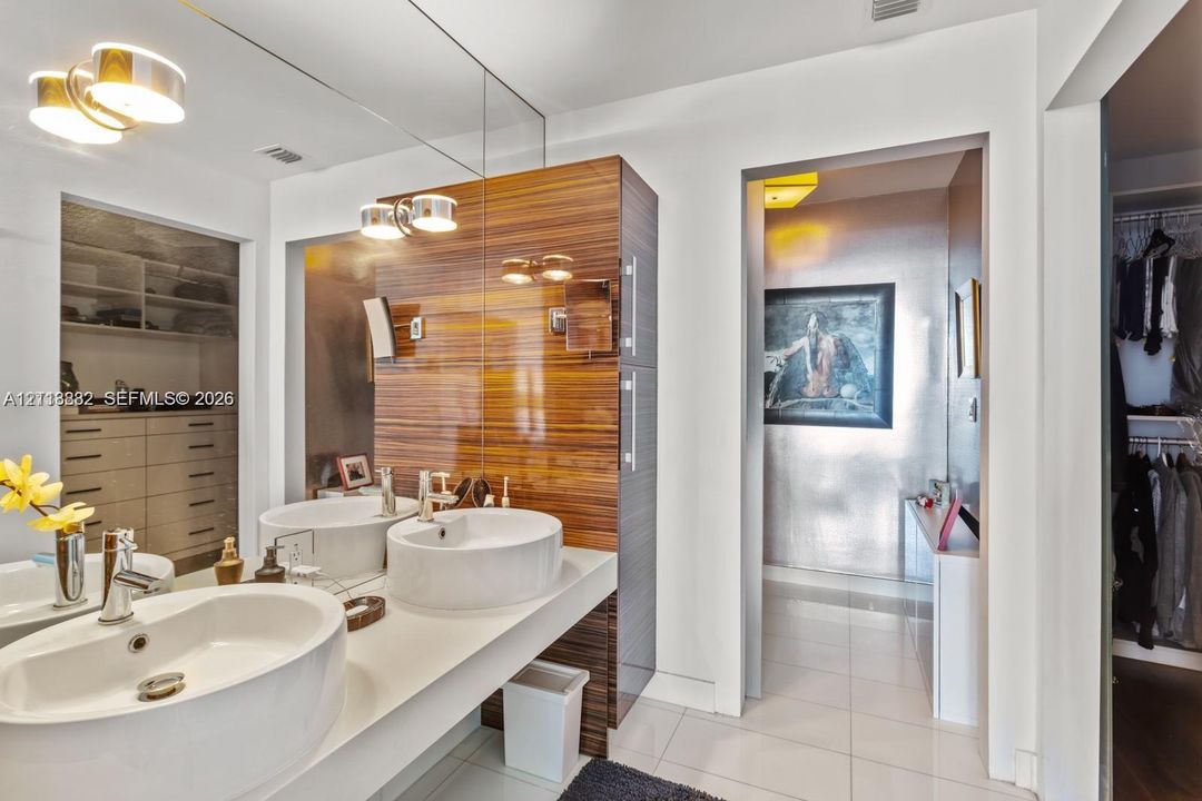 Dual-sink vanity with white basin bowls, polished chrome faucets, wall-to-wall mirror, and high-gloss wood-finish cabinetry
