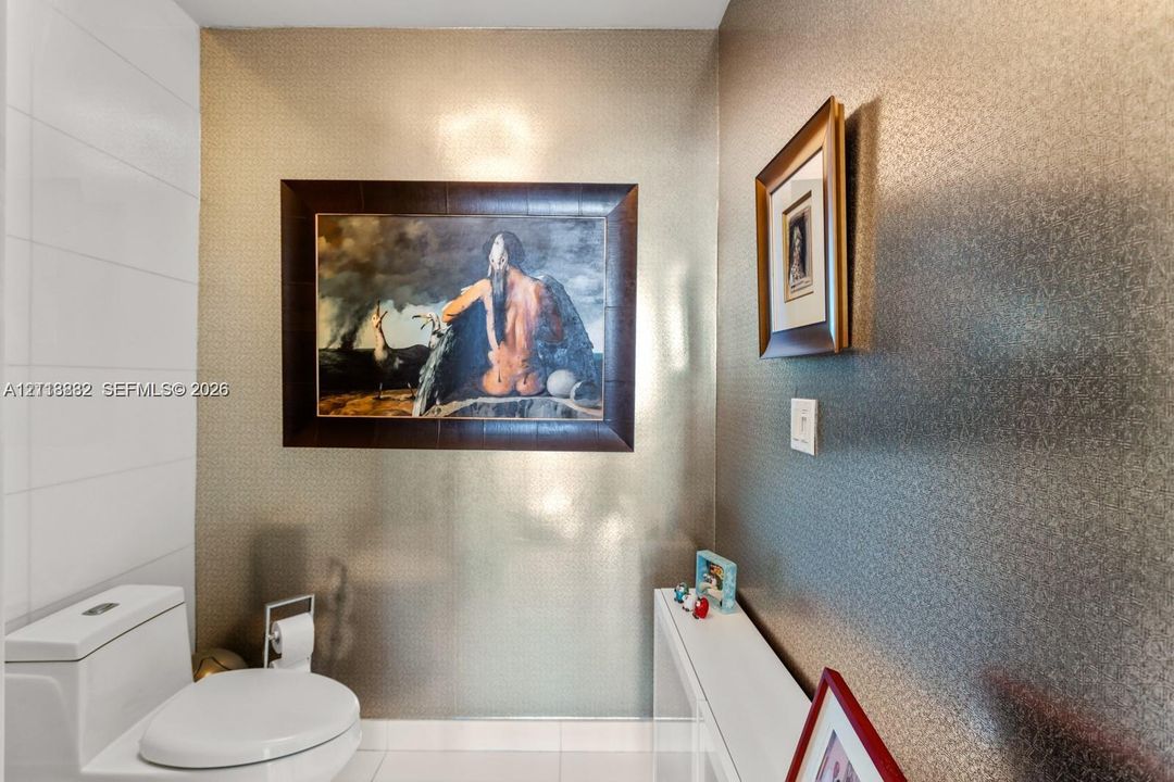 Restroom featuring metallic textured wall coverings, gloss-finish wall tile, and a white dual-flush toilet
