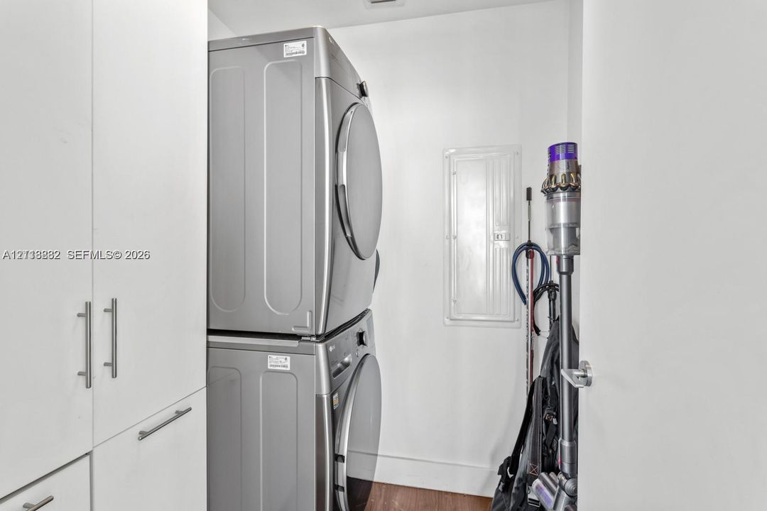 Laundry space featuring floor-to-ceiling white cabinetry with brushed nickel hardware and a stacked stainless steel laundry unit