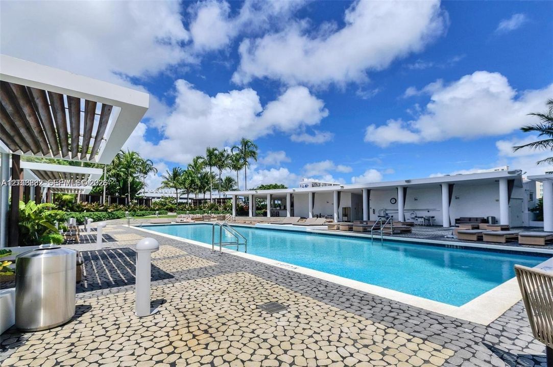 Swimming pool area featuring a rectangular pool, stone-paver decking, metal pergola structures, and covered pavilion space supported by cylindrical columns