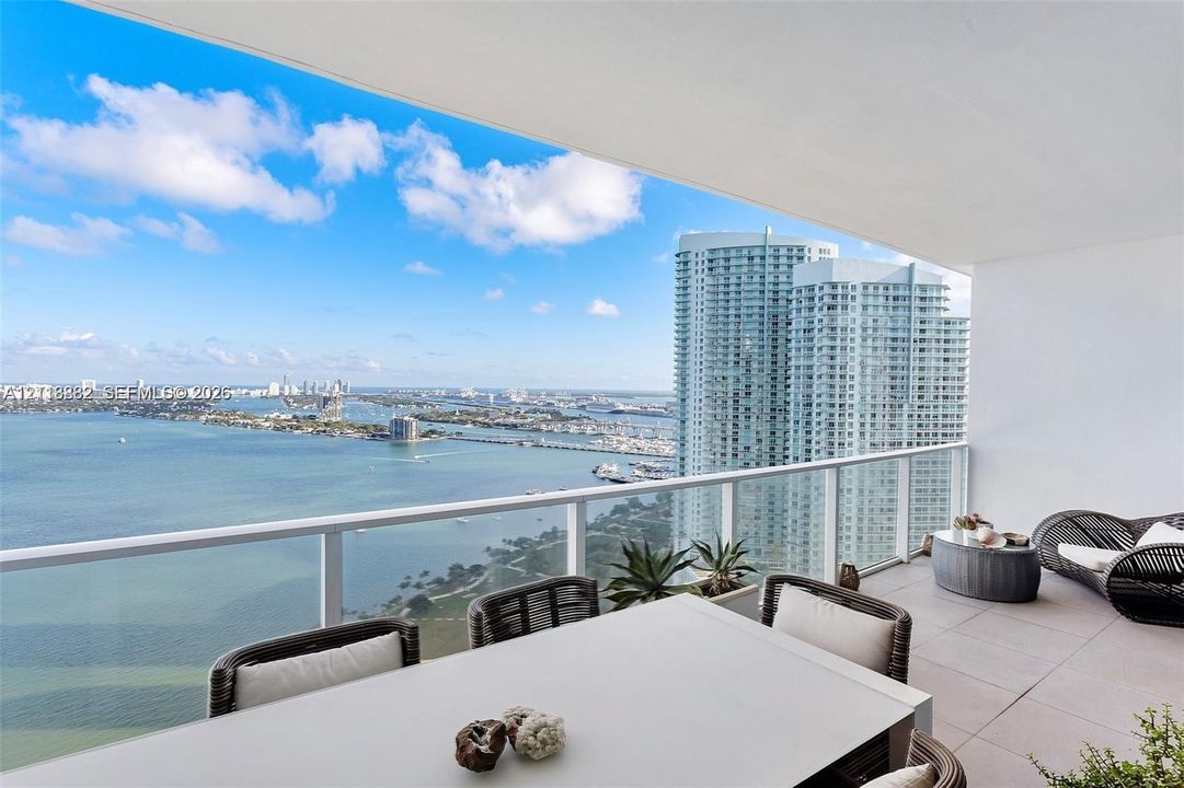 Covered balcony featuring expansive water and city skylines, glass paneled railings, and neutral tile flooring