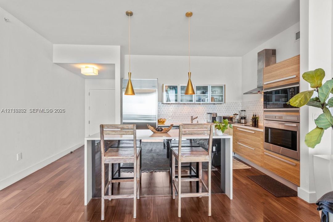 Kitchen featuring stainless steel appliances, wood-finish cabinetry, geometric backsplash, wood-finish flooring, and dual hanging pendant lights