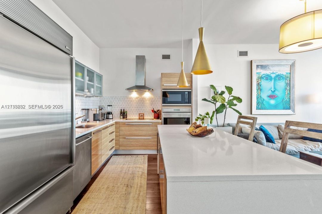 Kitchen featuring light-tone wood-finish cabinetry, a large quartz-topped island, stainless steel appliances, a chimney-style range hood, and geometric tile backsplash