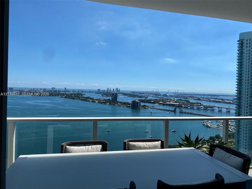 Covered balcony featuring white structural framing, tempered glass railings, and expansive coastal horizon