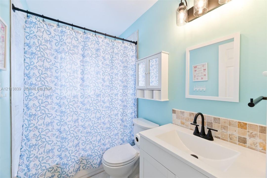 Bathroom featuring a vanity with a white countertop, matte black faucet, wall-mounted storage cabinet, and stone tile backsplash