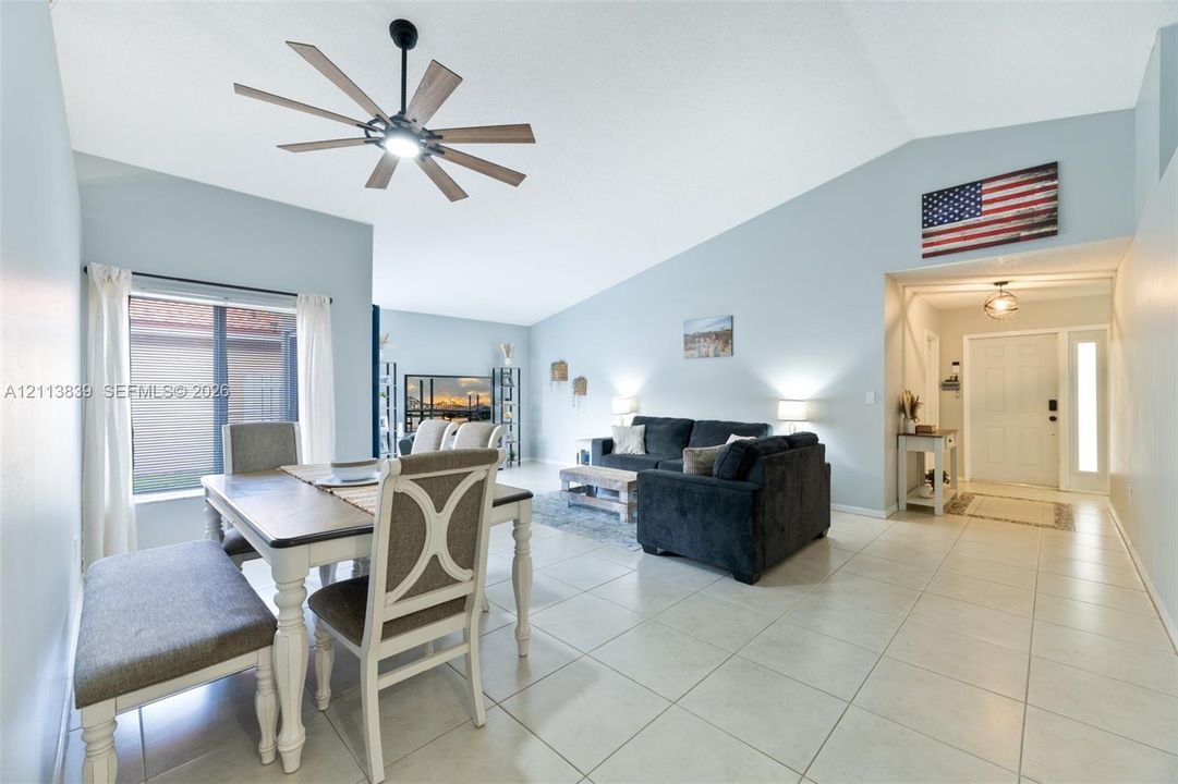 Vaulted ceilings, large-format tile flooring, multi-blade ceiling fan with integrated lighting, and a front entry door featuring a vertical glass sidelight