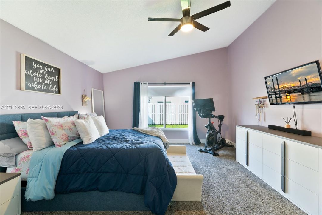 Vaulted ceilings, neutral carpeting, ceiling fan with integrated lighting, and wall-mounted television console