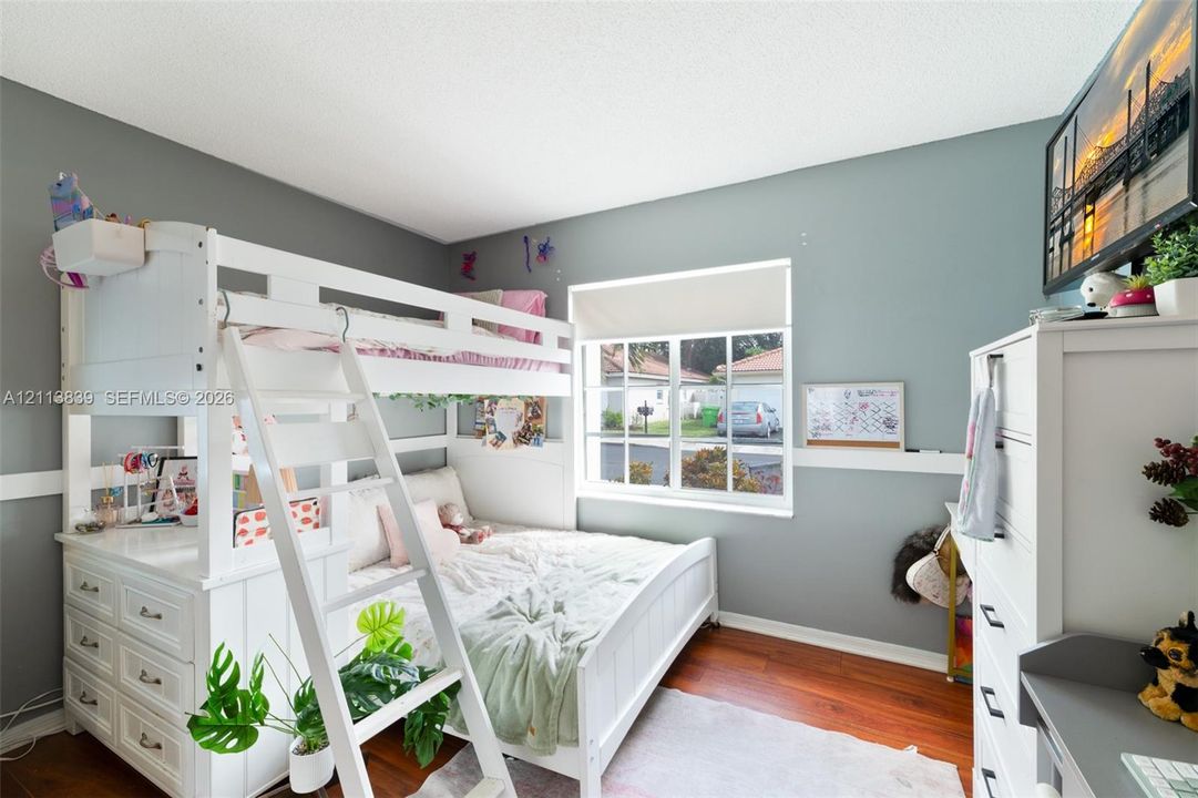 Bedroom featuring wood-finish flooring, a multi-pane window with a roller shade, and horizontal wall trim