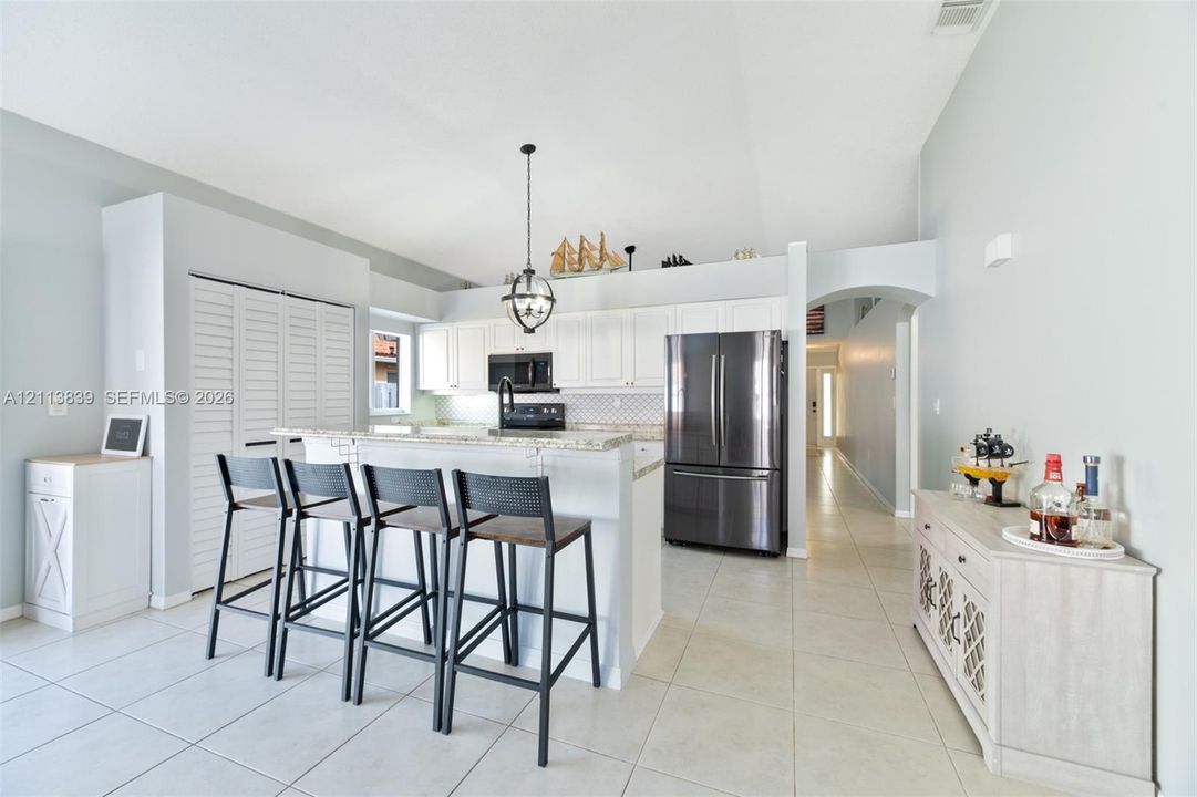 Kitchen featuring white cabinetry, stone countertops, stainless steel appliances, a center island with a stone-top breakfast bar, and tile flooring